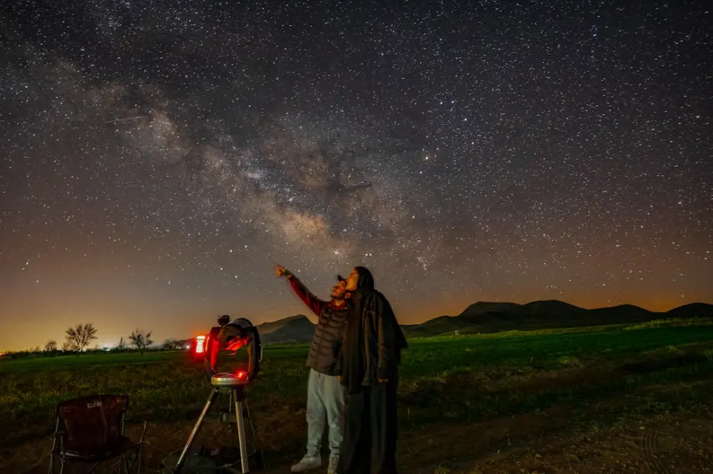 A man standing next to a telescope looking at the stars, illustrating learning astronomy
